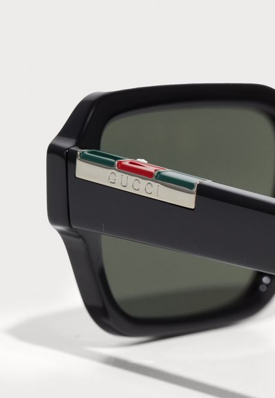 Lunettes de soleil noires avec des verres teintés, dotées d'une touche verte, rouge et blanche sur les branches et d'un détail logo métallique "GUCCI".