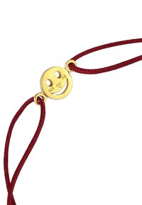 Goldfarbener Smiley-Gesichtsanhänger mit gravierten Markierungen, der an einem roten geflochtenen Band befestigt ist und ein einfaches, rundes Design aufweist.