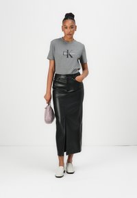 Pilkas medvilnės marškinėliai su "Calvin Klein" logotipu, juoda dirbtinės odos sijonas su įpjova, derinami su baltais lengvais bateliais ir maža violetine rankine.