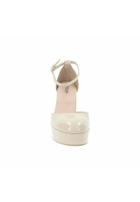 Pumps beige in vernice con tacco alto, cinturino alla caviglia, punta rotonda, superficie lucida e suola a pianta spessa.