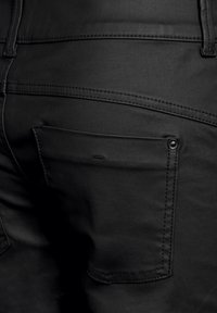 Svarta denimjeans med en bakficka som har en rund form, detalj med överstygn och en metallknäppning. Mjuk textur, figursydd design.