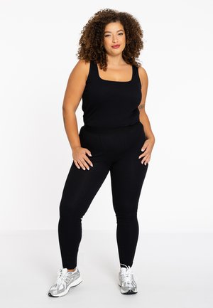 Zwarte tanktop met vierkante halslijn, gecombineerd met zwarte leggings. Heeft een soepele stof, een getailleerd ontwerp en witte sportschoenen.