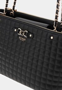 Borsa a tracolla in pelle nera trapuntata con hardware color oro, chiusura a zip e doppie catene per la spalla. Presenta una placca con logo sul davanti.