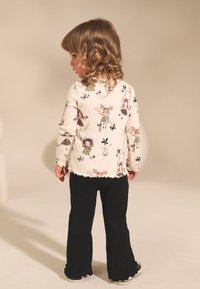 Chemise à manches longues crème avec motifs floraux et filles, associée à un pantalon évasé noir. Présente des bords festonnés et une texture de tissu douce.
