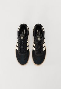 Černé sportovní boty se třemi bílými pruhy, texturovaným svrchním materiálem a podrážkou z gumové pryže. Na jazyku je logo.