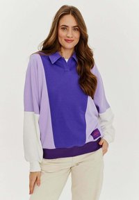 Fioletowa i jasnoliliowa długorękawowa koszulka polo z białym rękawem. Posiada ściągacz u dołu i metkę po prawej stronie.