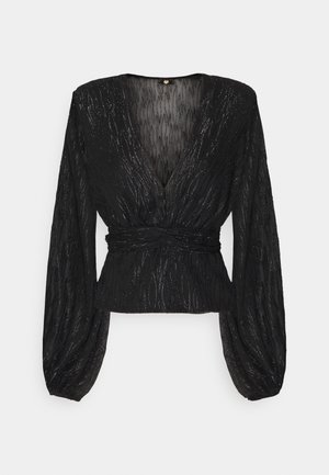 Blouse noire à manches longues avec un col en V profond, taille cintrée et un motif texturé subtilement scintillant, avec des manches légèrement bouffantes.