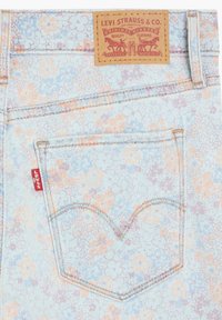 Jeans de mezclilla azul claro con un patrón floral en tonos durazno y púrpura. Presenta una etiqueta de cuero marrón y una pequeña etiqueta roja de Levi's en el bolsillo.