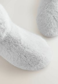 Pehmeät, karvaiset tohvelit valkoisissa ja harmaan sävyissä, joissa on pyöristetty varvasosa ja teksturoitu pinta lisälämmön ja mukavuuden takaamiseksi.