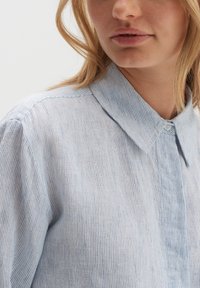 Light blue striped shirt with a classic collar, featuring a button closure, and made of lightweight fabric. Soft texture with a relaxed fit.