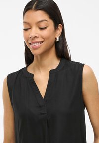 Mustat hihattomat blouse, jossa on hillitty V-pääntie, valmistettu sileästä kankaasta. Mallissa on rento istuvuus ja vähäisesti ompelutietoja.