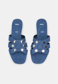 Sandales en denim à bride triple avec des accents circulaires en argent, dotées d'une semelle plate et d'un tissu texturé bleu.
