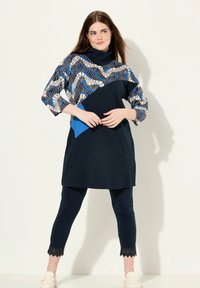 Marintröja med blå och vita geometriska mönster, korta ärmar, i kombination med marinblå leggings med spetsdetaljer vid anklarna.