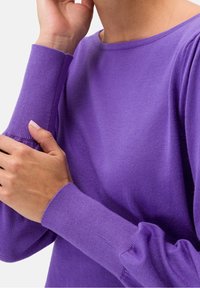 Pull en tricot violet avec un col rond et des poignets côtelés. La texture est lisse, présentant une silhouette ajustée et des détails froncés aux manches.