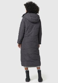 Lang, mørkegrå pufferjakke med hætte, vandret quiltet design, sidelommer og et logo patch nær kanten. Glat, isoleret tekstur.
