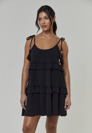 Czarna sukienka na ramiączkach bez rękawów, z trzema warstwami falban, regulowanymi wiązanymi ramiączkami ozdobionymi frędzlami i drewnianymi koralikami. Lekka tkanina o miękkiej fakturze.