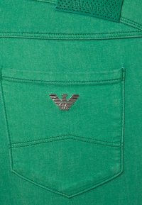 Grön denimtyg med en bakficka som har en silverfärgad Armani Jeans-logotyp och en texturerad läderetikett. Rena sömmar genomgående.