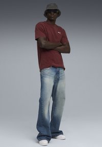 Mørkerød bomulds-T-shirt med Puma-logo, kombineret med lyseblå flagrende jeans med kædedetalje og hvide sneakers. Bucket hat og solbriller.