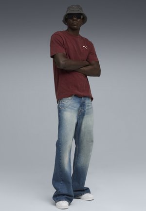 Mørkerød bomulds-T-shirt med Puma-logo, kombineret med lyseblå flagrende jeans med kædedetalje og hvide sneakers. Bucket hat og solbriller.
