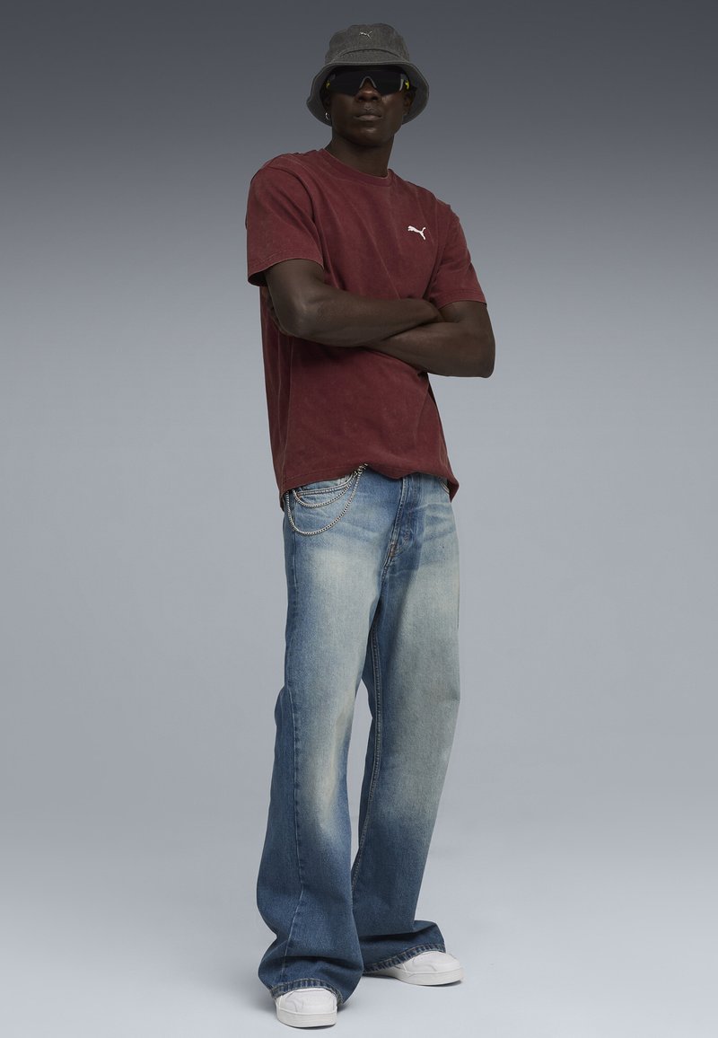 Mørkerød bomulds-T-shirt med Puma-logo, kombineret med lyseblå flagrende jeans med kædedetalje og hvide sneakers. Bucket hat og solbriller.