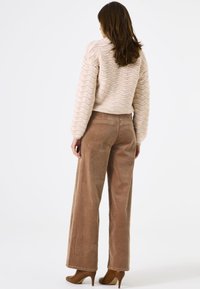Gehaakte crème trui met golfpatroon, gecombineerd met lichtbruine hoge taille corduroy broek en bruine hakken.
