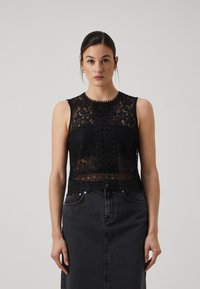 Svart blonde ermeløs topp med intrikate blomster mønstre, rund halslinje og en delikat heklet kant. Kombinert med et svart denim skjørt.