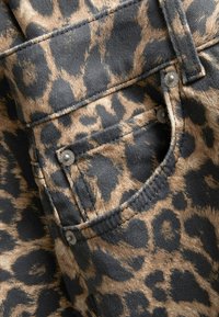 Leopard print denim fabric featuring a back pocket with silver hardware and visible stitching. The design includes dark spots on a tan background.