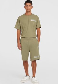 Olijfgroen katoenen t-shirt en shorts set. Ontspannen pasvorm met een ronde hals en zijzakken. Voorzien van een wit tekstlogo op de borst en op de shorts.