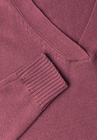 Gros plan d'un pull tricoté mauve montrant un poignet côtelé et un détail texturé au col en V.