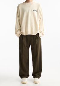 Kermainen neulepaita pyöreällä pääntiellä ja kirjailulla, yhdistetty tummiin oliivinvihreisiin leveälahkeisiin housuihin ja valkoisiin tennareihin.