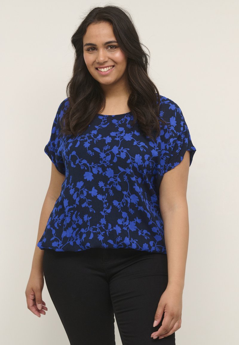 Top azul marino con un patrón floral en azul brillante, de manga corta y un corte holgado. Combinado con pantalones negros.