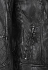 Schwarze Lederjacke mit einer auffälligen Reißverschlusstasche und silbernem Zubehör, strukturierten Oberflächen und kontrastierenden Nähten entlang der Nähte.