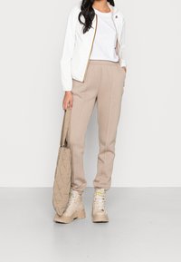 Hvid letvægtsjakke med gyldne detaljer, ensfarvet hvid t-shirt, beige sweatpants og beige snørebåndsstøvler, parret med en struktureret totebag.