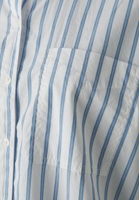 Striped shirt in white and light blue, featuring a buttoned front, a pocket on the left chest, and a smooth cotton texture.