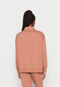 Överdimensionerad sweatshirt i mjuk, dammig rosafärgad tyg. Har en hög krage, nedhasade axlar och en avslappnad passform med ribbade muddar och fåll.