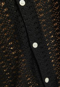 Czarny kardigan na szydełku z kwiatowym wzorem, teksturowanym materiałem i białymi guzikami wzdłuż przodu.