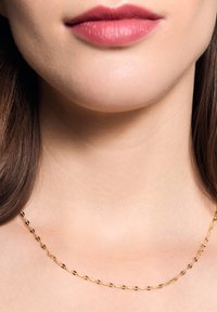 Złoty naszyjnik z łańcuszkiem o owalnych ogniwach, z spiralnym wzorem i subtelnymi czarnymi akcentami, spoczywający na gładkiej powierzchni skóry.