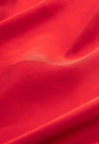 Rød stof med en glat tekstur, der udviser en subtil glans. Materialet folder sig naturligt og reflekterer lyset med en blød, ensartet farve.