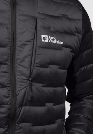 Zwarte pufferjack met een gewatteerde textuur, een ritszak en een logo-detail op de borst. De stof lijkt lichtgewicht en waterafstotend.
