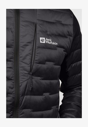 Zwarte pufferjack met een gewatteerde textuur, een ritszak en een logo-detail op de borst. De stof lijkt lichtgewicht en waterafstotend.
