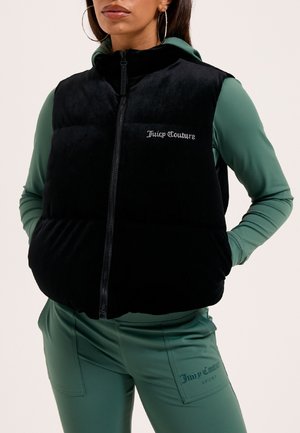 Gilet in pile nero con zip frontale, caratterizzato da un design imbottito e il logo "Juicy Couture" in strass. Indossato sopra un tuta verde.