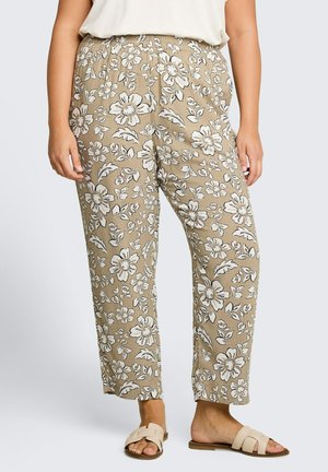 Beige pants with white floral print worn with white top and beige slip-on sandals on a person standing against plain background.