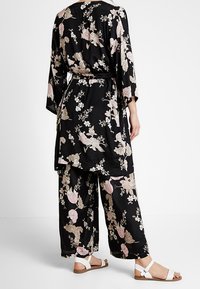 Sort blomsterkimono med lange ærmer og matchende bukser med vide ben. Har pink og cremefarvede blomsterprint. Bruges med hvide sandaler.