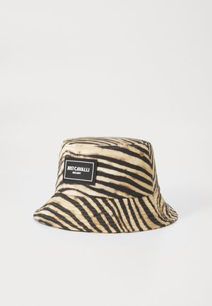 Chapeau seau en tissu avec un motif en rayures zèbre noir et beige. Comprend une étiquette rectangulaire noire avec du texte blanc.