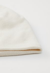 Berretto di maglia color crema chiaro, realizzato in un tessuto morbido e textured con orlo ripiegato. Design semplice e liscio, privo di accenti o fantasie aggiuntive.