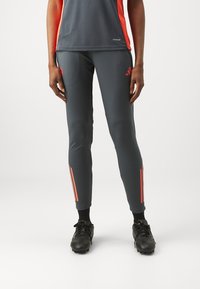 Pantalons de sport gris avec des bandes d'accent orange sur les côtés, dotés d'une coupe slim et fabriqués à partir d'un matériau lisse et extensible.