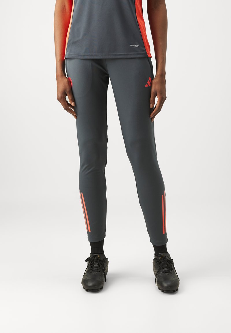 Pantalons de sport gris avec des bandes d'accent orange sur les côtés, dotés d'une coupe slim et fabriqués à partir d'un matériau lisse et extensible.