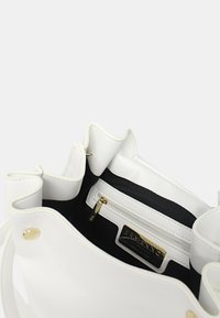 Borsa a mano in pelle bianca con interni neri. Presenta una tasca con zip e un hardware con accenti dorati. Finitura morbida e testurizzata con parte superiore arricciata.