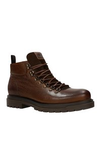 Bruine leren wandelschoen met een gestructureerde afwerking, bruine veters, bronzen veterogen en een stevige rubberen zool. Enkelhoogte met een versterkte hiel.