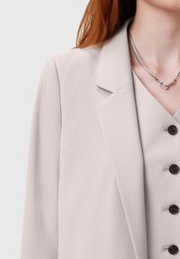Gaiši rozā žakete no mīksta auduma, ar ieliktu atloku, vienrindu aizdari un tumšām pogām.